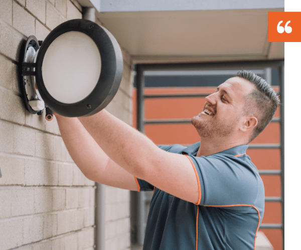 Smiling Marrickville electrician installing a wall light fixture.